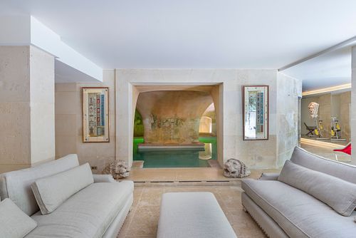 Salon avec canapés gris et vue sur la piscine intérieure sous les voûtes à Saint-Germain-des-Prés. Photographie d'architecture intérieure par Nicolas Karadimos.