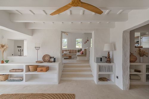 Salon ouvert et lumineux avec banquettes intégrées, escalier et vue sur l’extérieur dans la finca Son Fonoll à Minorque. Photographie par Nicolas Karadimos.