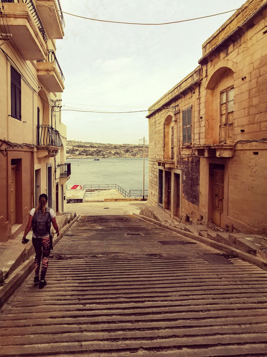 Traveller walking down a historic street towards the waterfront in a Mediterranean town.