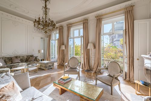 Grand salon haussmannien dans un immeuble de 1880 à la Place de l’Etoile, Paris, avec lustre en cristal, canapés élégants et vue sur le balcon. Photographie d’architecture intérieure par Nicolas Karadimos.