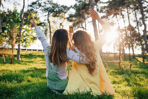Two young women sitting on grass hugging rear view