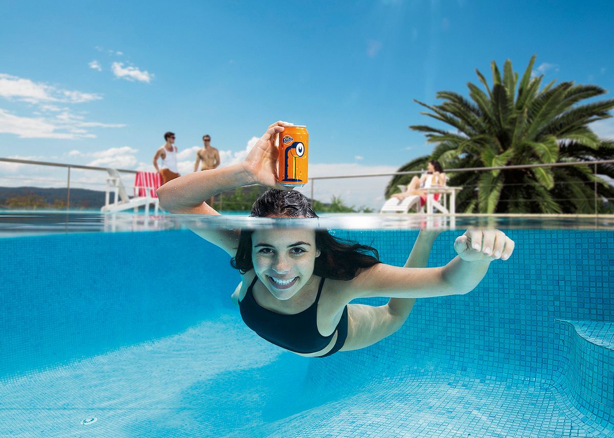 Girl in swimming with fanta can as a periscope in a pool. Photography shoot.
