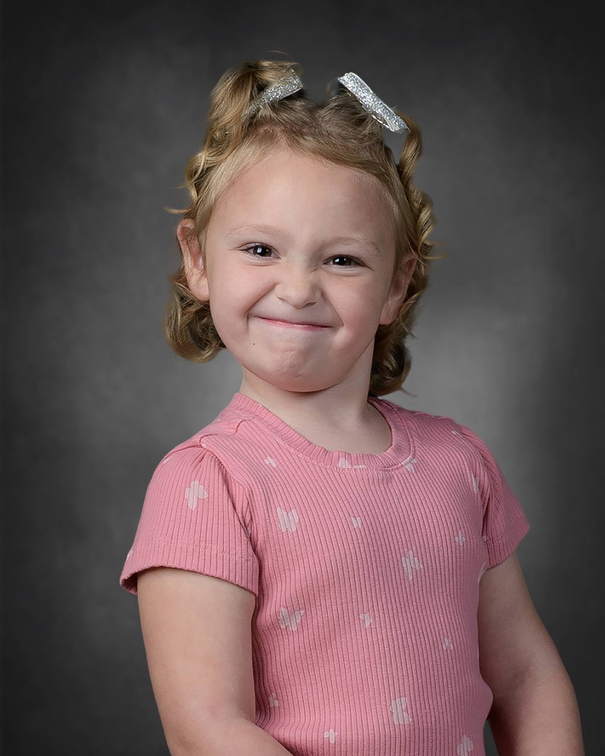 Early learning center child posing and making a playful face wearing pink shirt on black lighted background