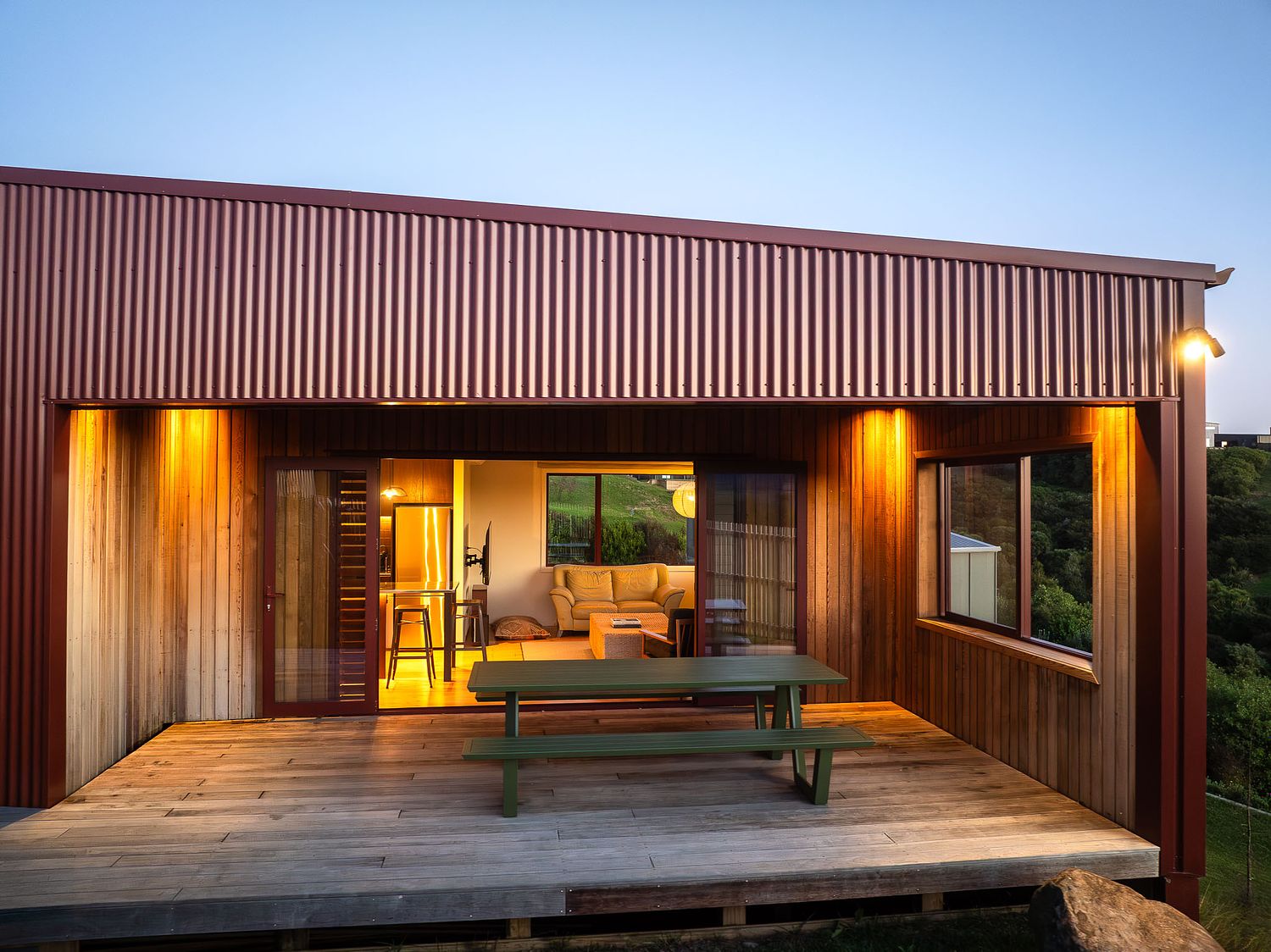 Twilight real estate photography highlighting the illuminated wooden deck and outdoor dining area of a Rangitahi Peninsula home, shot by Flax Cove Studio