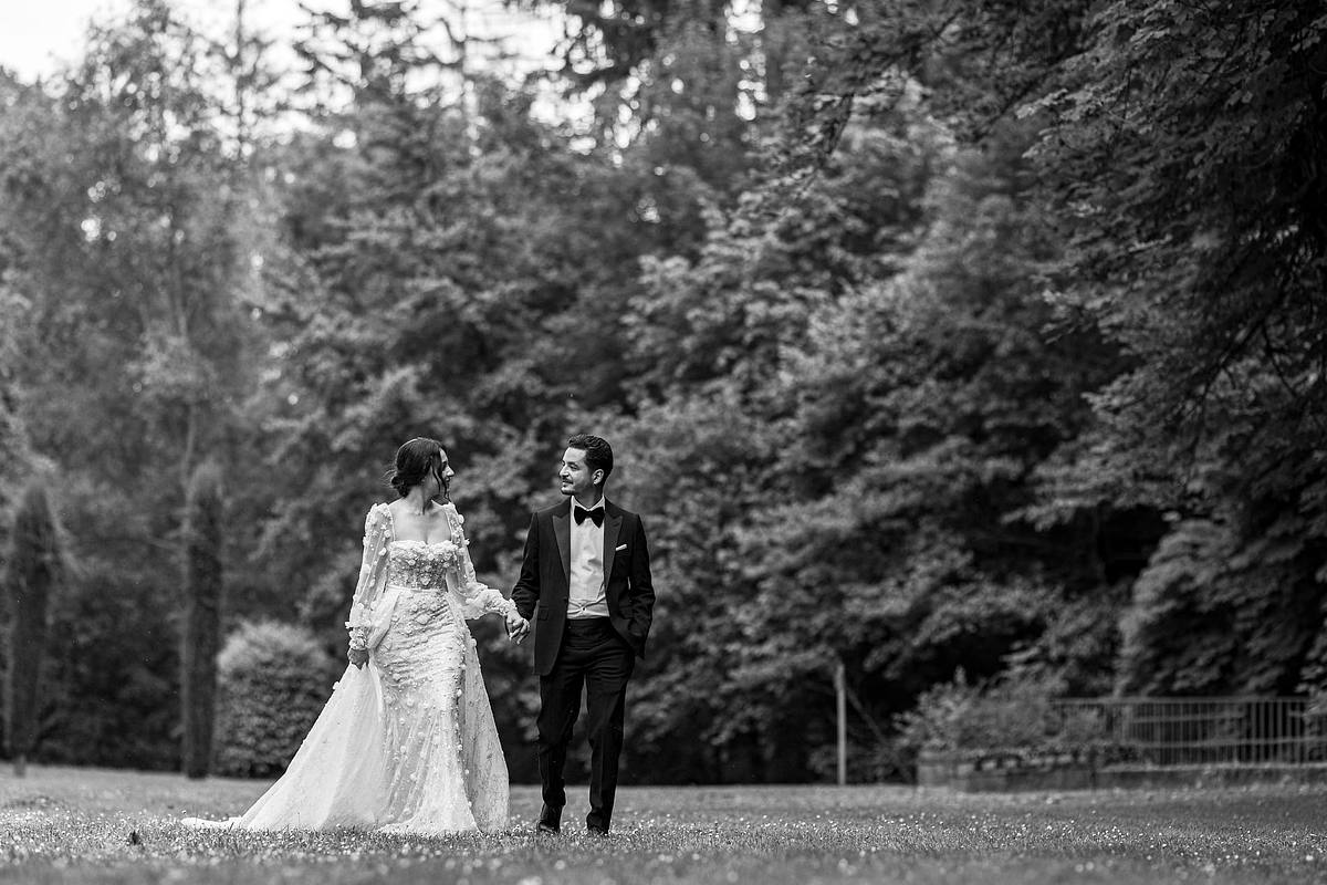 Un couple de jeunes mari&eacute;s marche main dans la main dans un parc tranquille, encadr&eacute; par la nature, immortalis&eacute; dans une photographie romantique en noir et blanc par Sebastien CLAVEL Photographe mariage Lyon