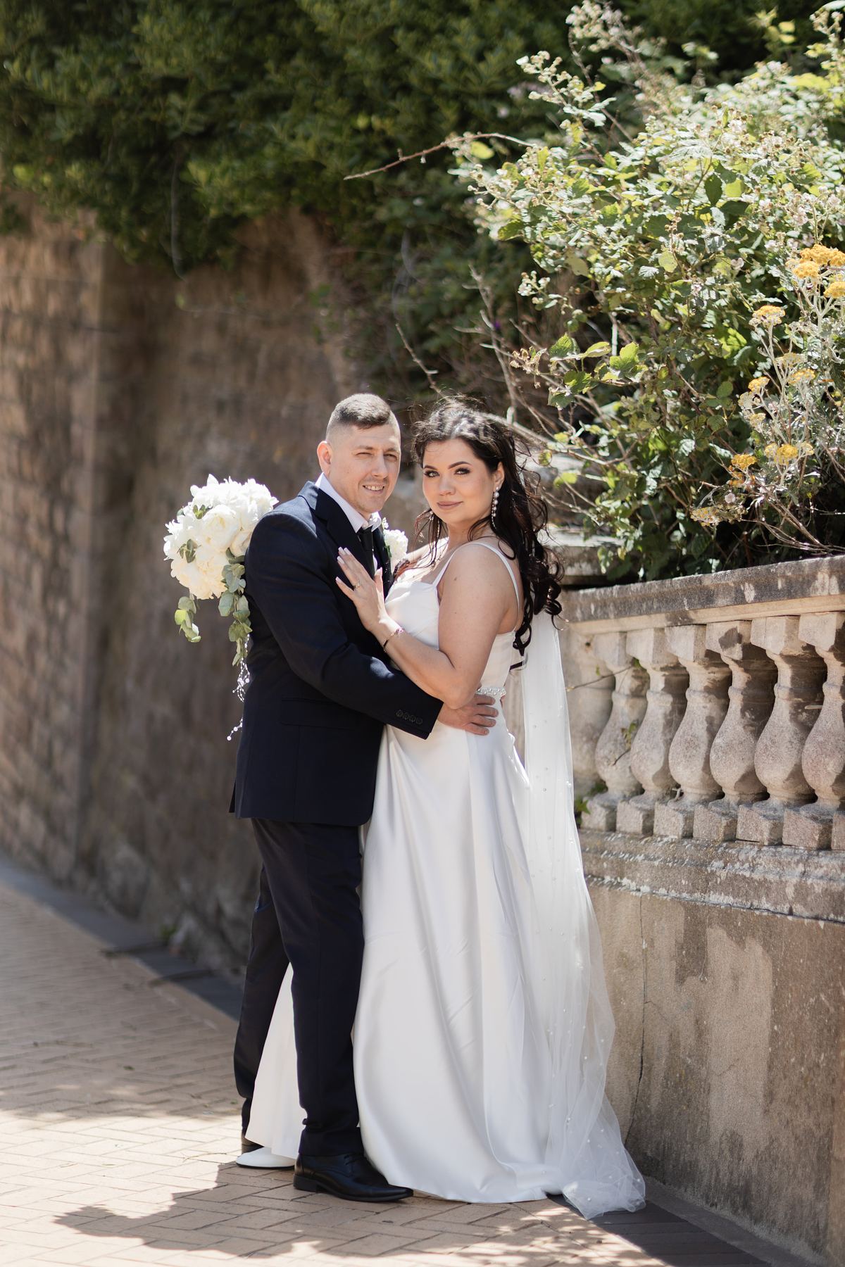 Full-length portrait of bride and groom beside a stone balustrade at Barry Island, South Wales