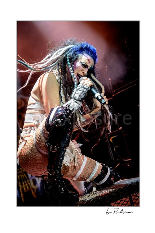 Vertical color image of Calico Cooper of Beasto Blanco singing into a microphone in a fierce live performance pose, with long dreadlocks, dramatic stage makeup, and stage smoke behind her