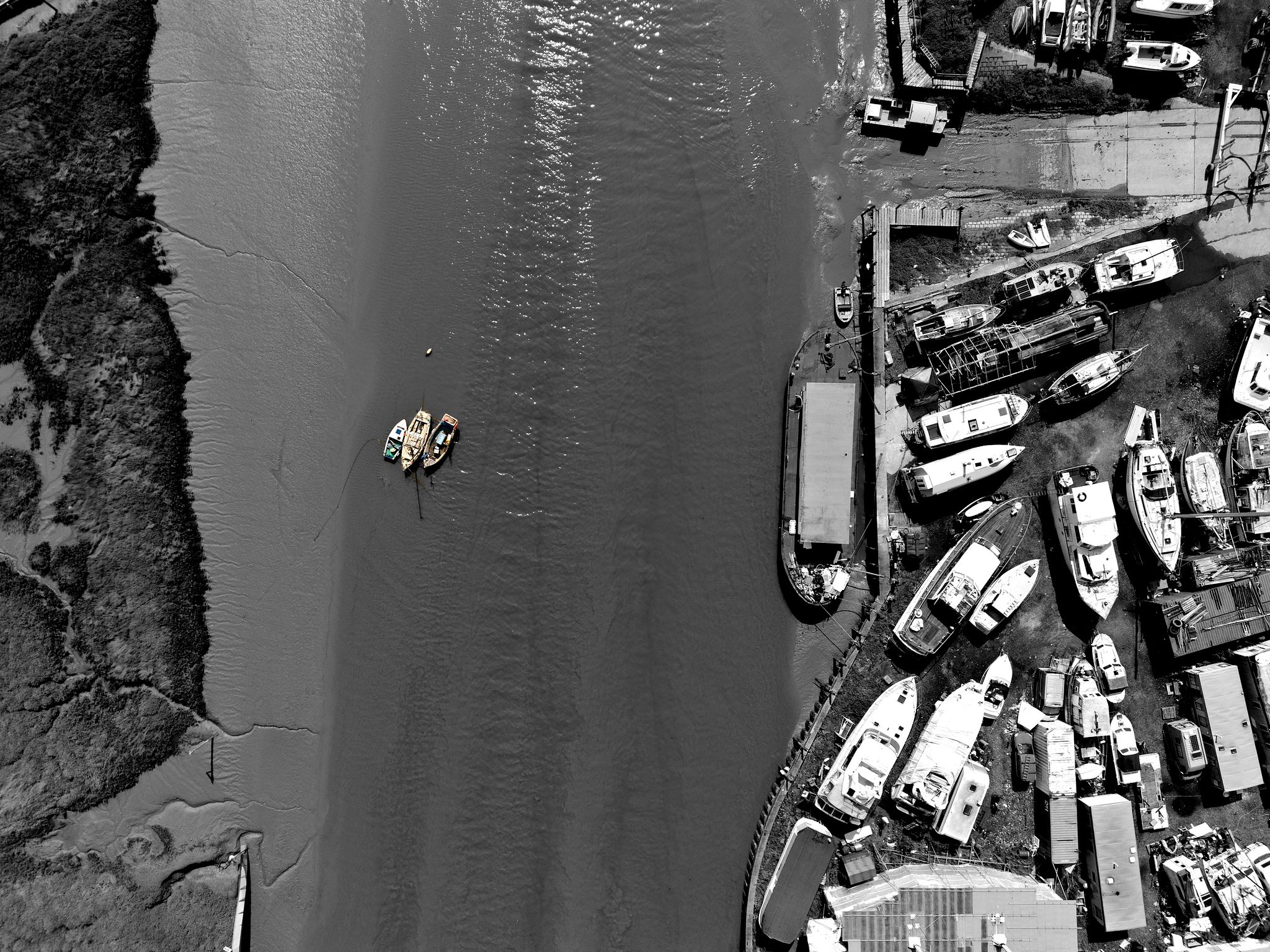 Three coloured boats anchored in Benfleet Creek beside a boatyard, fine art aerial drone photography
