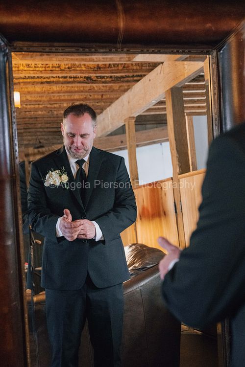 A groom fixes his cuff link in front of a mirror