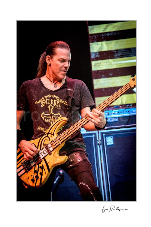 Vertical color image of Perry Richardson of Stryper performing live with bass guitar on stage