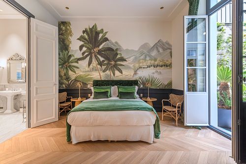 Chambre à coucher d’un appartement haussmannien de 400 m² rue du Faubourg Saint-Honoré avec grand papier peint panoramique tropical, lit en velours vert et vue sur le jardin. Photographie d’architecture intérieure par Nicolas Karadimos.