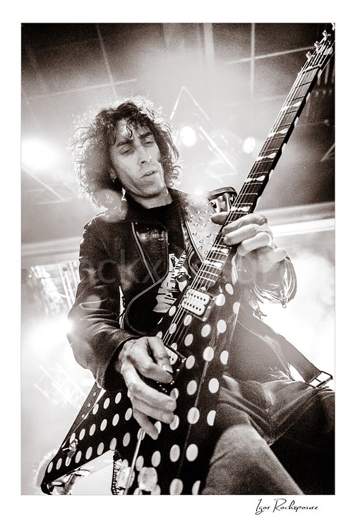 Vertical black and white image of Brent Woods playing guitar in a dramatic low-angle close-up under bright stage lights