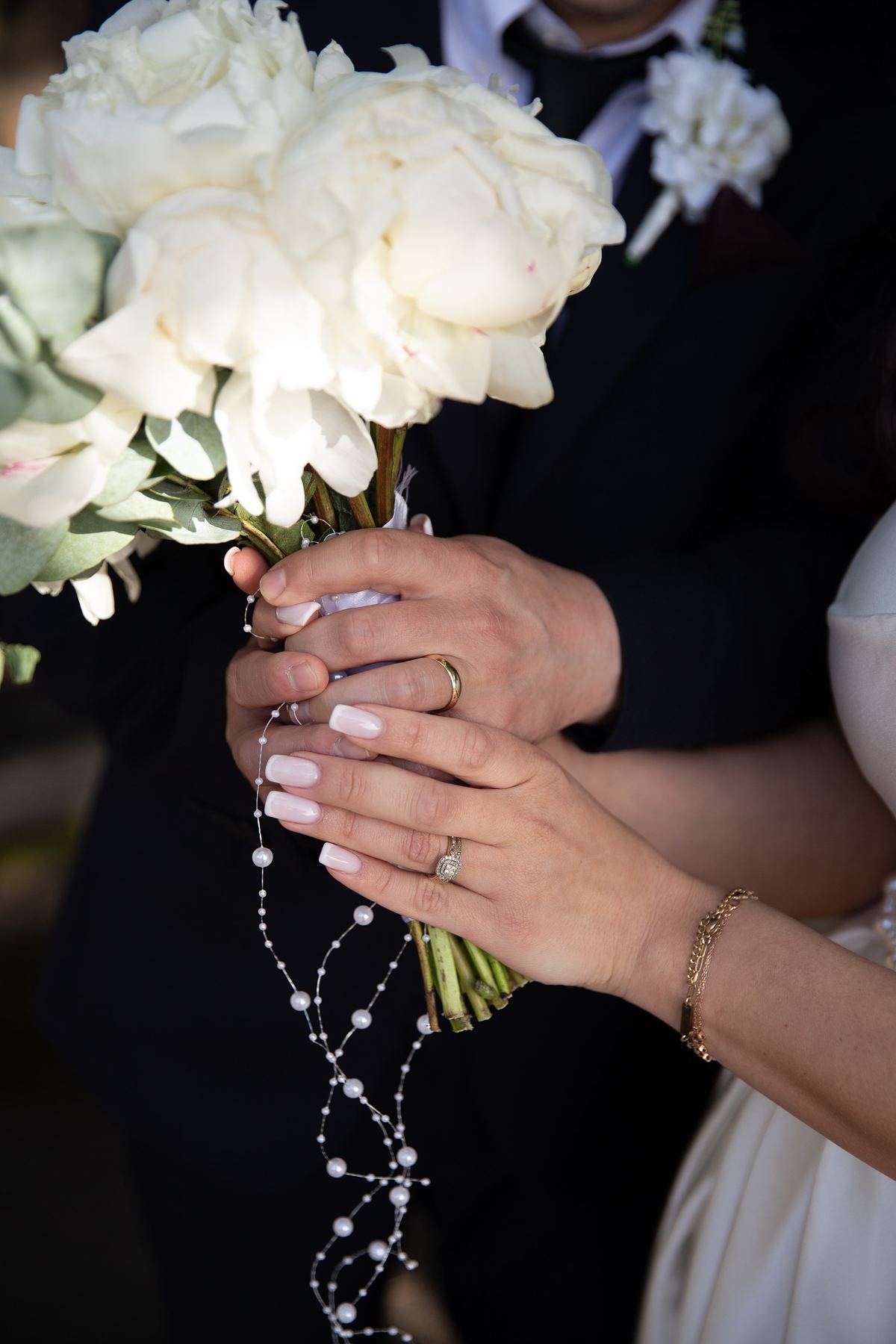 Close-up of bride holding white wedding bouquet with wedding rings visible