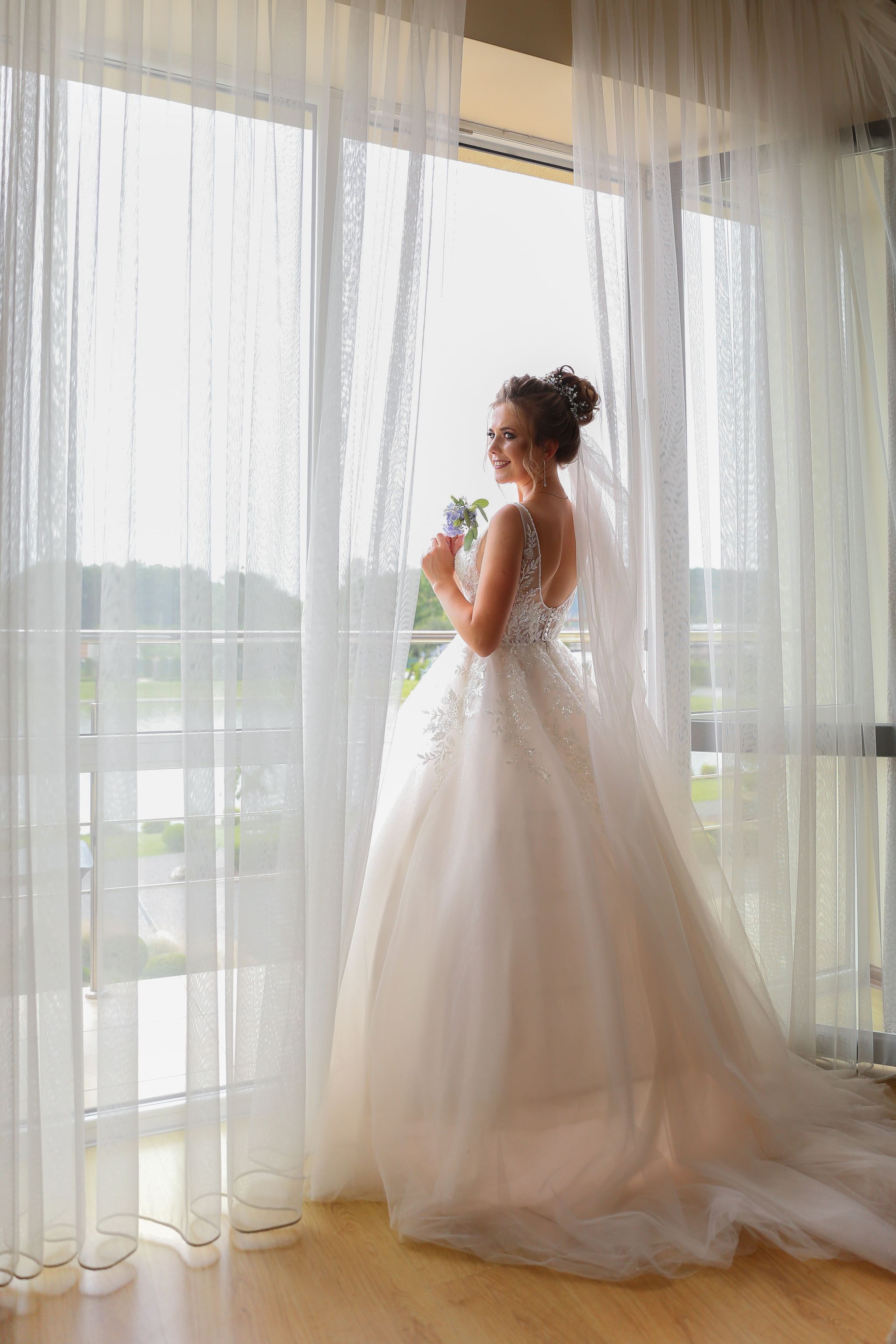 Bride standing by a window in her wedding dress before the ceremony