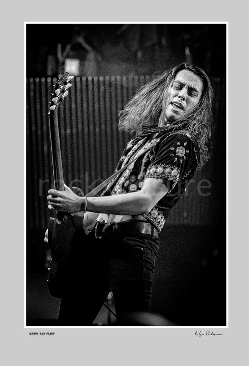 Vertical black and white image of Greta Van Fleet bassist Sam Kiszka performing live with his bass guitar