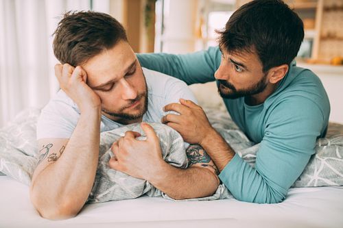 Sad man lying in the bed with his male partner. The partner hugg