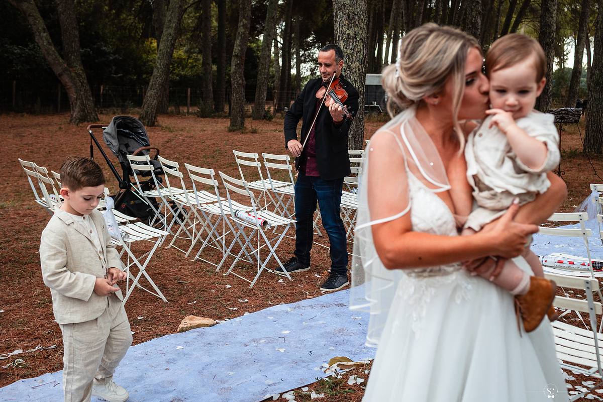 Mari&eacute;e partageant un moment affectueux avec son fils, sur fond de c&eacute;r&eacute;monie musicale, captur&eacute; avec art par S&eacute;bastien Clavel, photographe de mariage