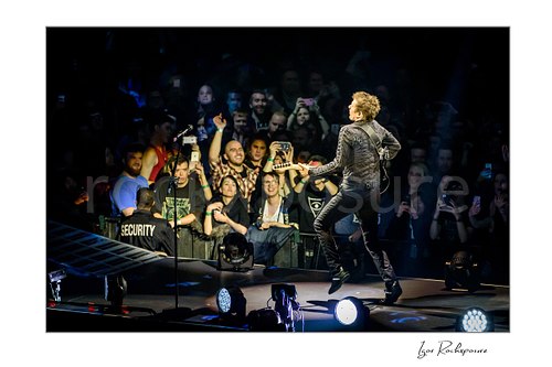Horizontal color image of Matt Bellamy of Muse leaping on stage with guitar before a packed arena crowd