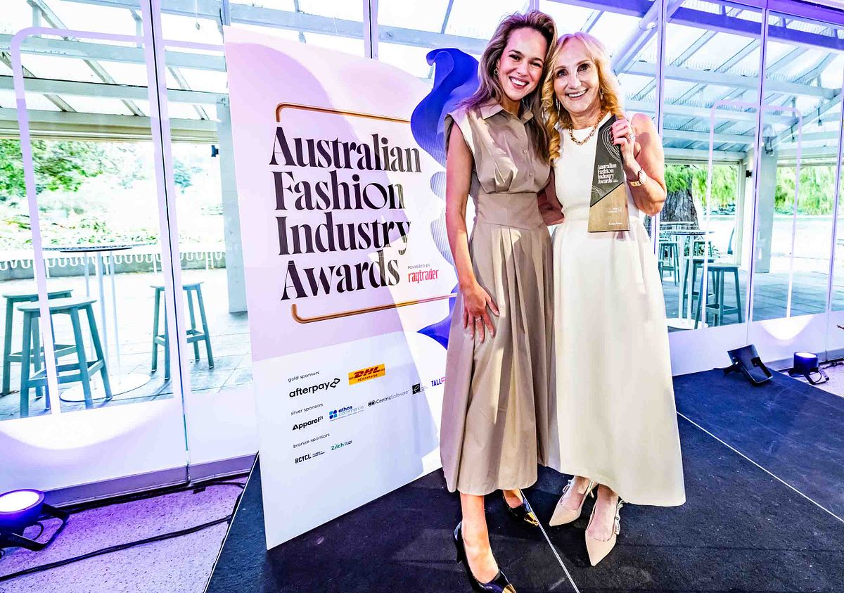 The host of the Australian Fashion Industry Awards hands a recipient an award on stage.