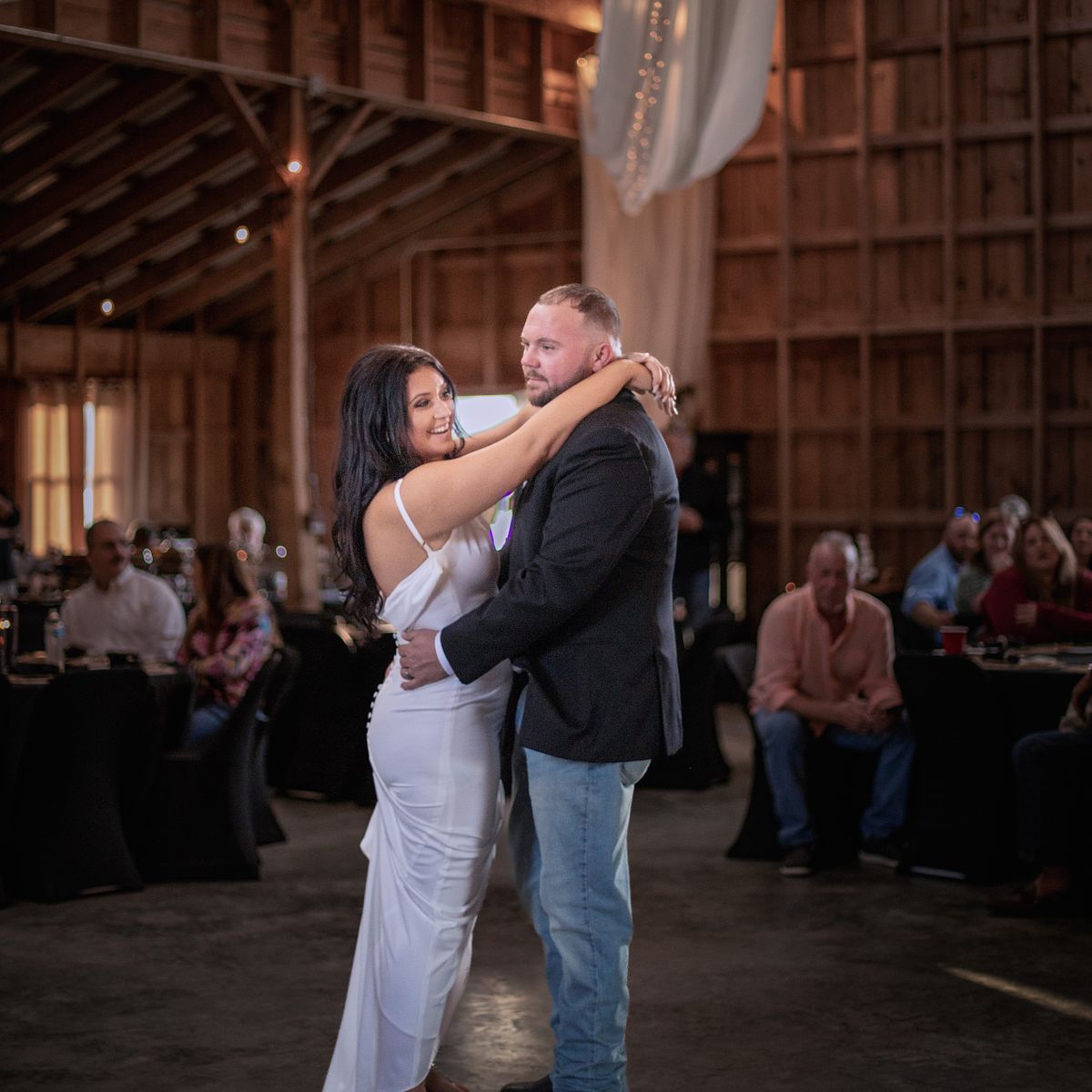 first dance inside cohee farm's rustic high ceiling barn. the bride is wearing a white satind dress, the groom, jeans and a blue blazer