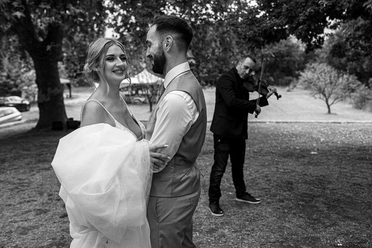 Mari&eacute;e et mari&eacute; souriants dansant sous les arbres au son d'un violon, captur&eacute;s par S&eacute;bastien Clavel, photographe de mariage &agrave; N&icirc;mes et en France