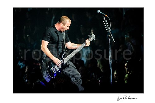 Horizontal color image of Mike Kroeger of Nickelback playing bass onstage beside a microphone stand during a live performance