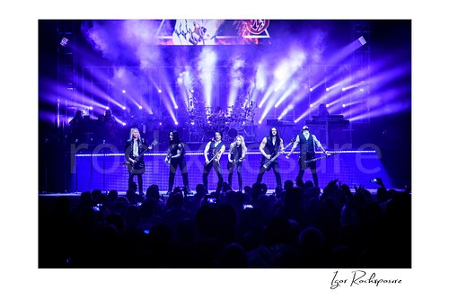 Horizontal color image of Trans Siberian Orchestra performing on stage with the full band under purple concert lighting