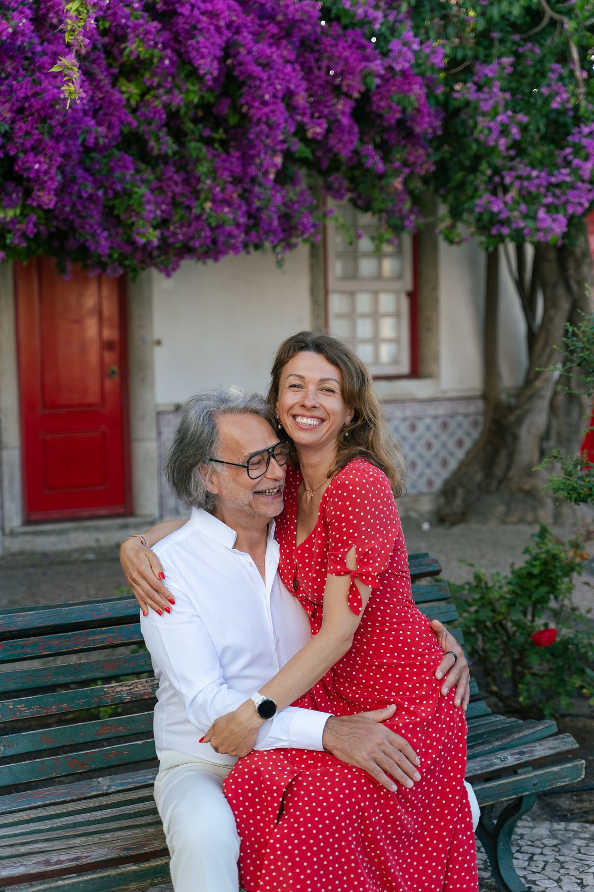 Couple posing beneath bougainvillea beside a red door in Lisbon