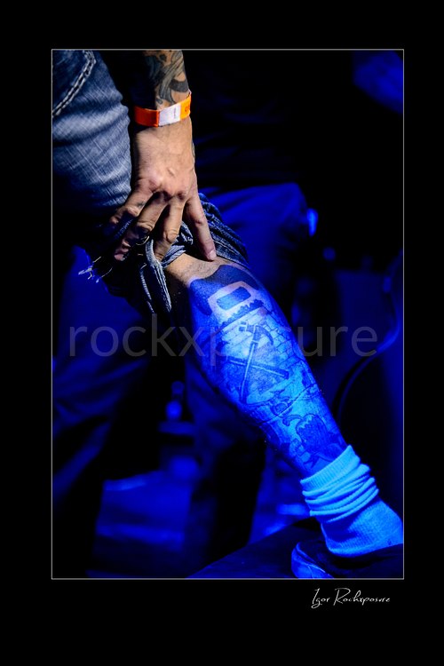 Vertical color image of Mike Portnoy’s leg tattoo in close-up under deep blue stage lighting