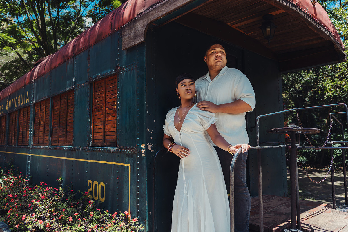 Engaged couple posing beside a vintage blue train carriage in Medellin