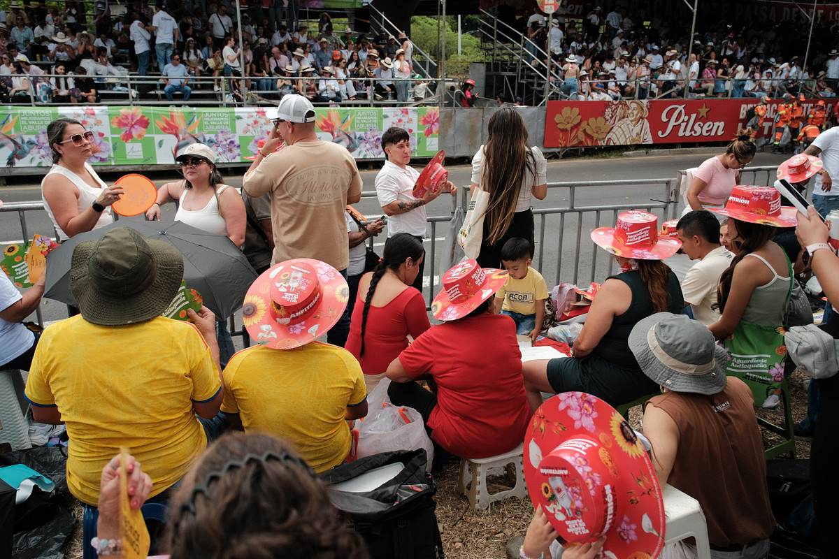 Público en las gradas con sombreros y abanicos viendo el desfile de la Feria de las Flores