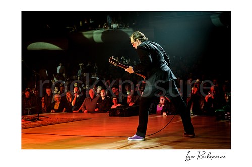 Horizontal color image of Joe Bonamassa performing live on stage with his guitar near the front of the crowd