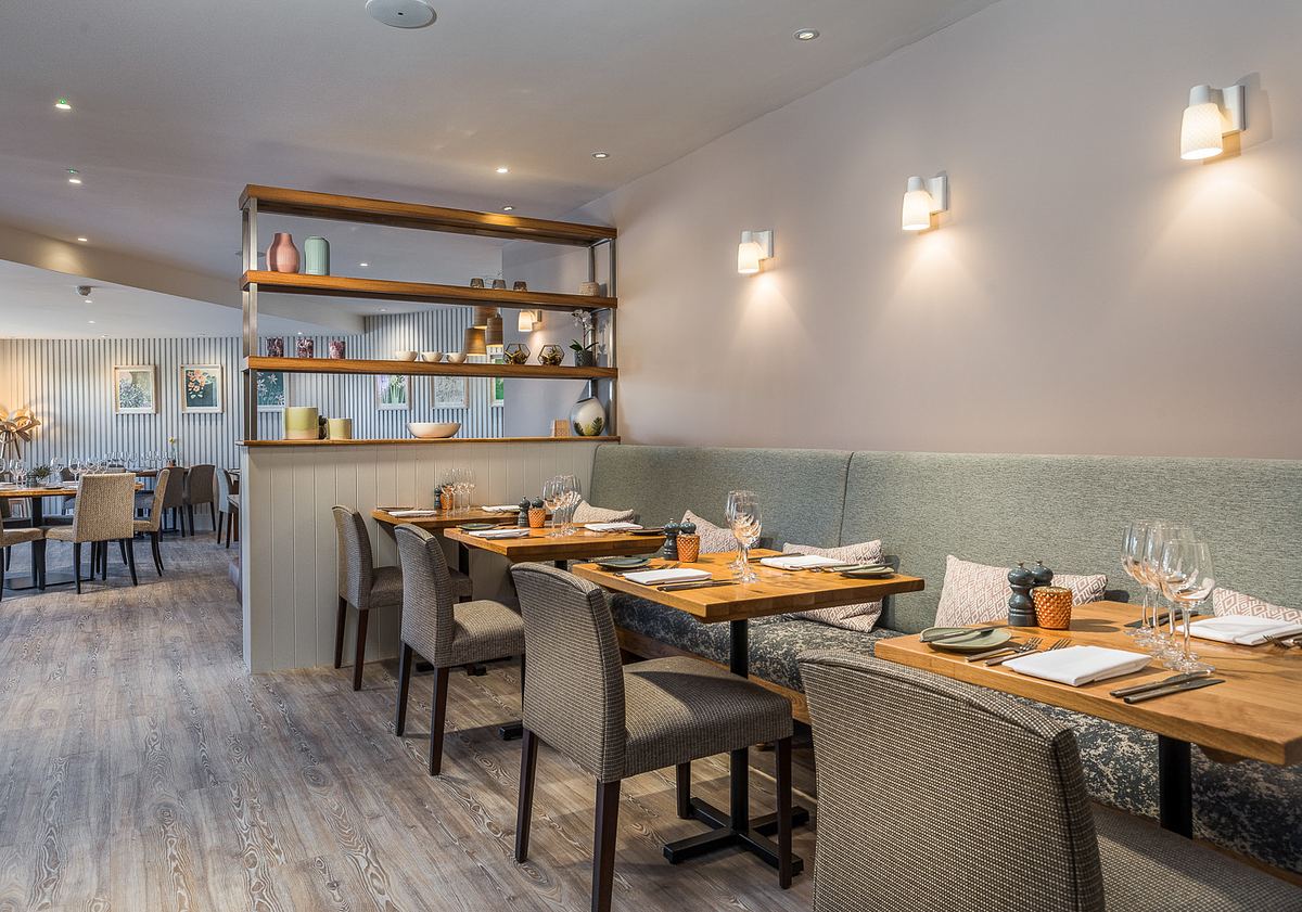 An interior of a hotel restaurant in Cornwall in the evening. Tables are laid, lights are on.