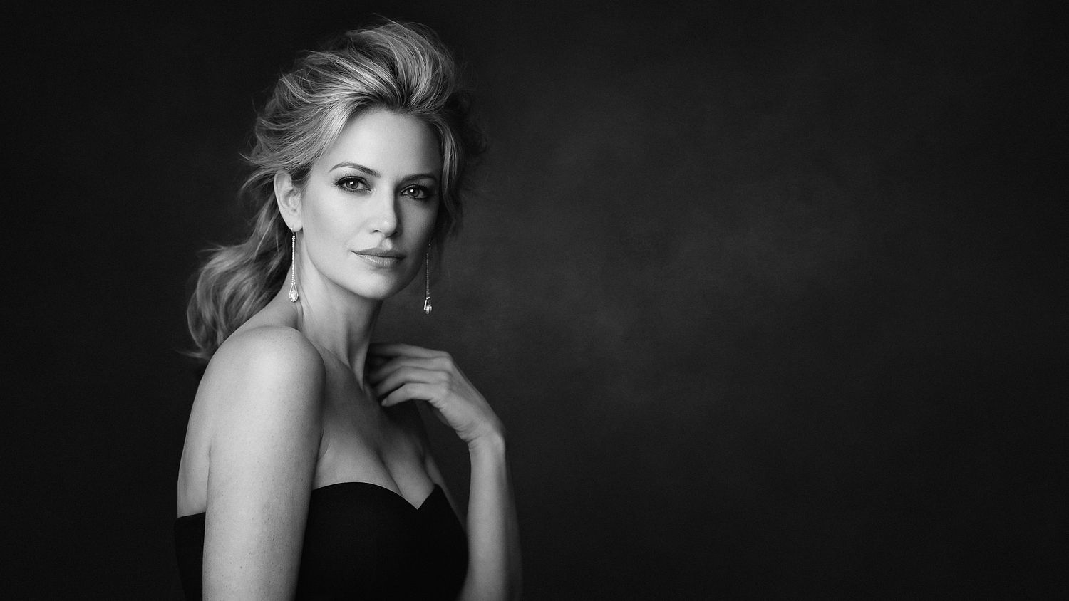 Elegant black and white studio portrait of a blonde woman in a strapless black dress on a dark background in Tallinn
