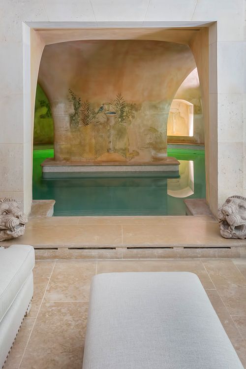 Vue encadrée de la piscine intérieure à Saint-Germain-des-Prés avec fresque murale, voûtes en pierre et têtes de lion sculptées. Photographie d'architecture intérieure par Nicolas Karadimos.