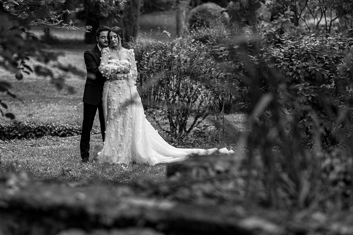 Portrait en noir et blanc des jeunes mari&eacute;s partageant un moment intime dans un jardin luxuriant, l'amour et la tendresse captur&eacute;s dans le regard de la mari&eacute;e par Sebastien CLAVEL Photographe mariage Lyon