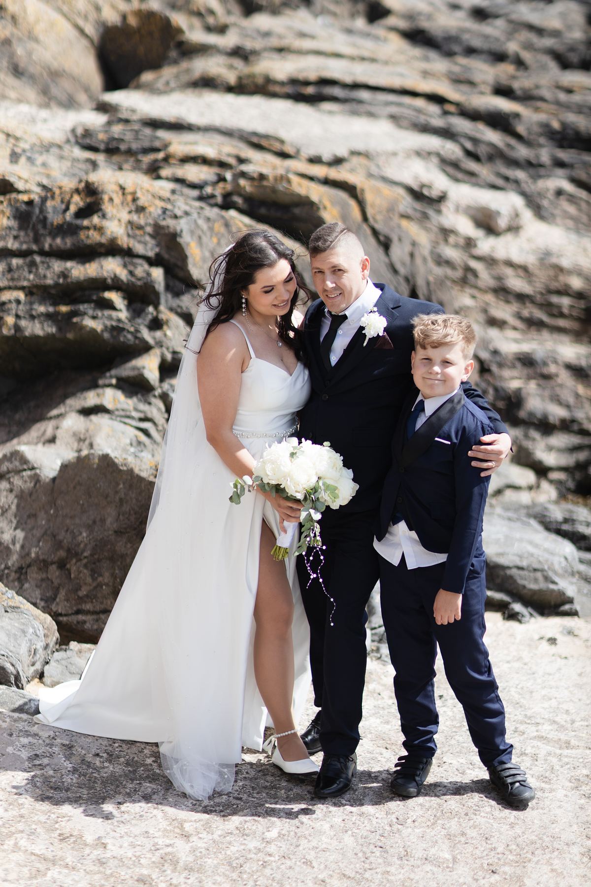 Bride and groom with a young boy on the rocky coast at Barry Island, South Wales