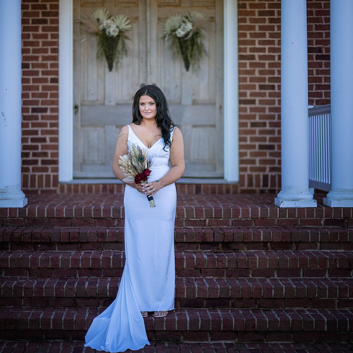 bride posing in front of the double doors at cohee barn in williamsburh, md