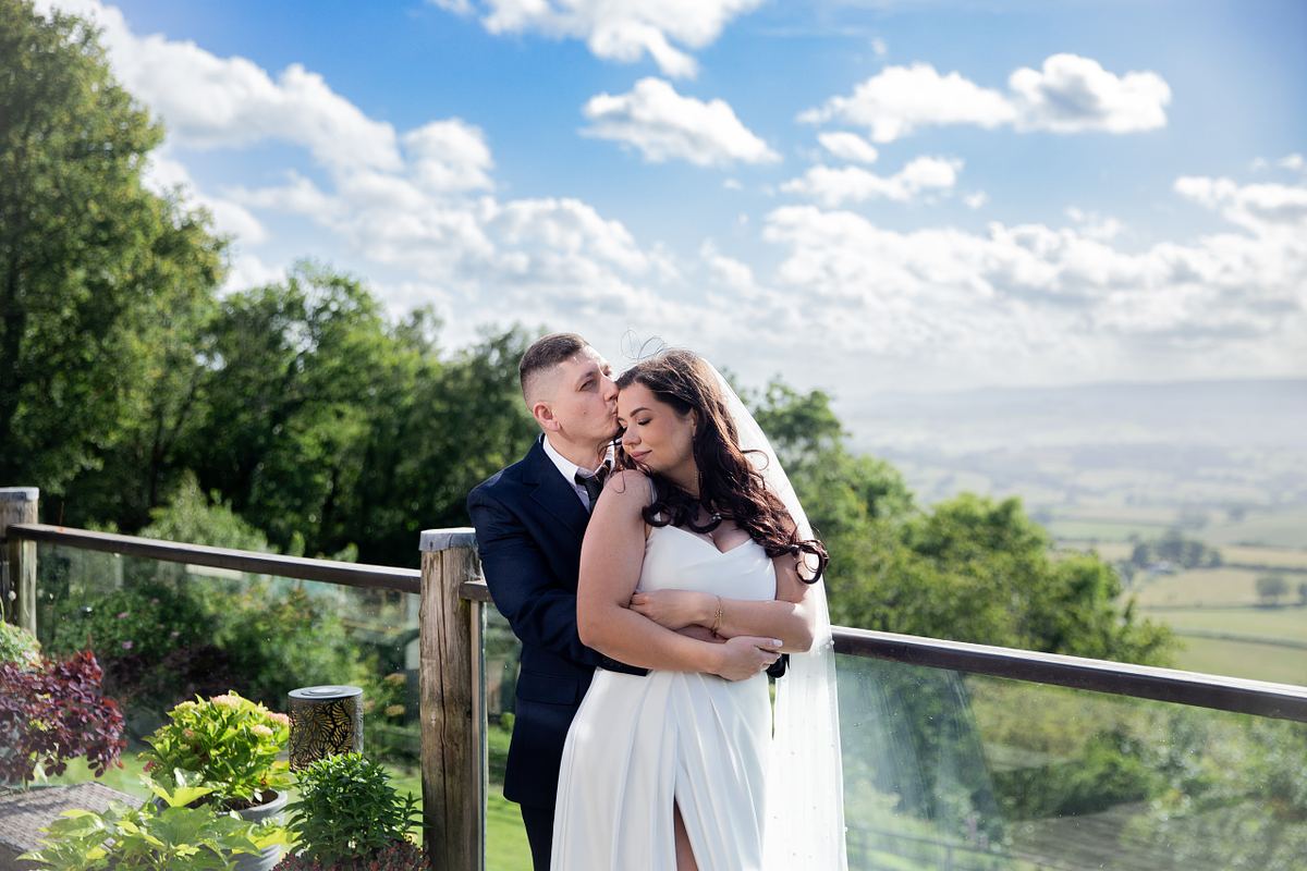 Groom kissing bride on a terrace overlooking the South Wales countryside