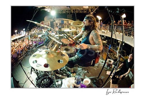 Mike Portnoy Live Concert Print  Horizontal color image of Mike Portnoy playing drums on stage at night in a wide fisheye concert scene with the crowd and ship deck behind him