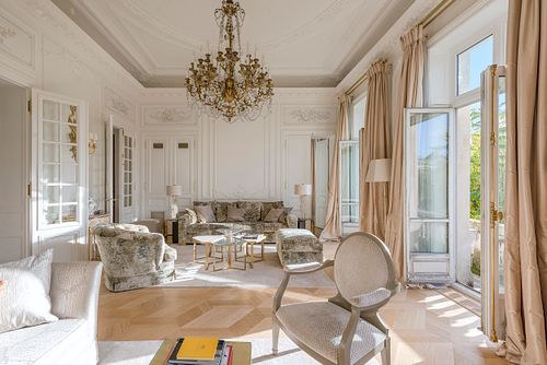 Grand salon haussmannien dans un immeuble de 1880 à la Place de l’Etoile, Paris, avec lustre en cristal, canapés élégants et vue sur le balcon. Photographie d’architecture intérieure par Nicolas Karadimos.