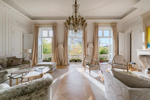 Grand salon haussmannien dans un immeuble de 1880 à la Place de l’Etoile, Paris, avec lustre en cristal, moulures au plafond et vue sur le balcon. Photographie d’architecture intérieure par Nicolas Karadimos.