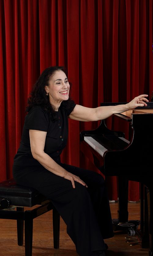 Myriam Birger seated at the piano before a recital, in a stage setting with a red curtain