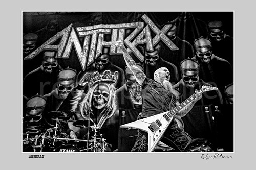 Horizontal black and white image of Scott Ian of Anthrax performing live on stage, raising one arm while playing guitar in front of the band’s dramatic skull-themed stage backdrop