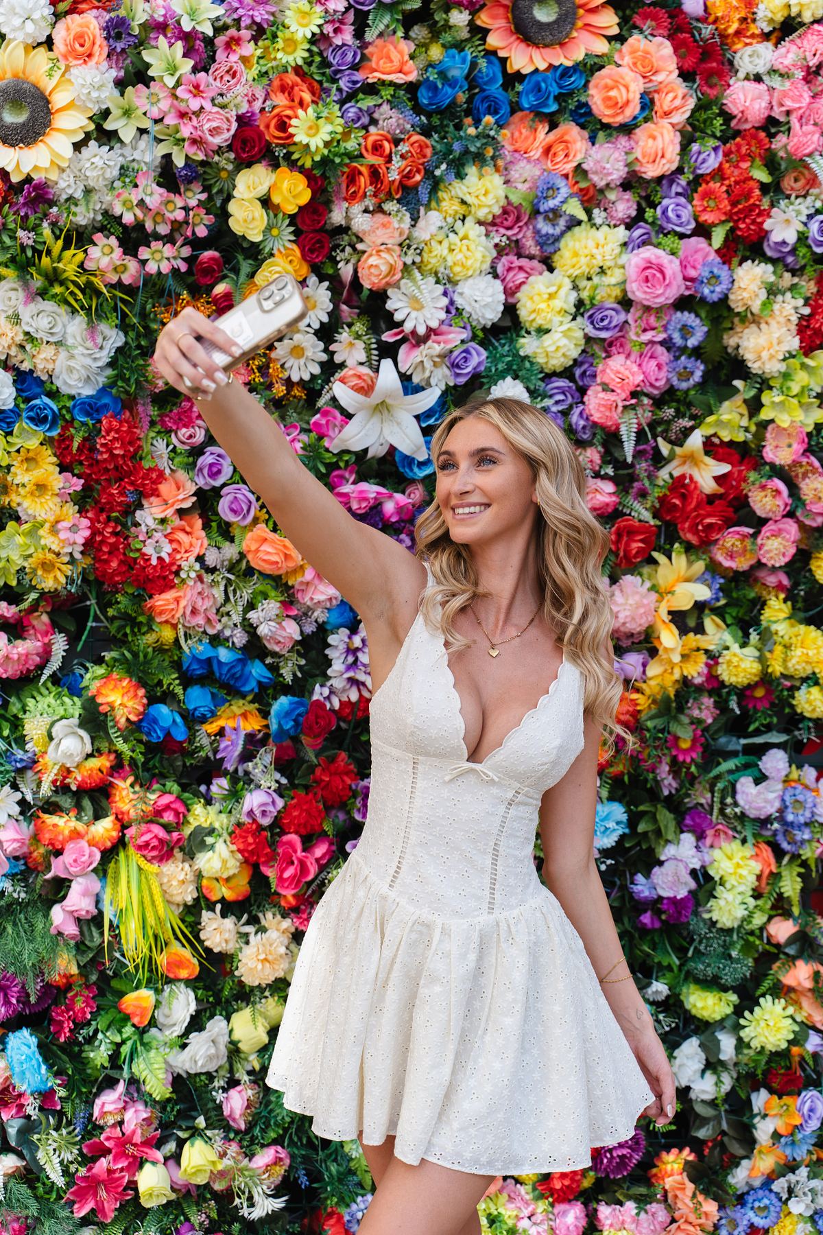 Woman taking a selfie in front of a colourful flower wall