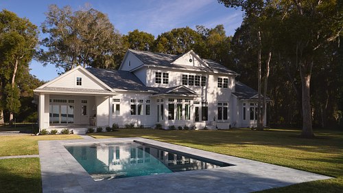 White Colonial-style estate in St. Johns County featuring a luxury pool and mature oak trees.