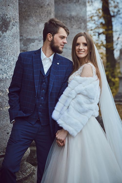 Bride and groom beneath the historic church columns in Pidhirtsi