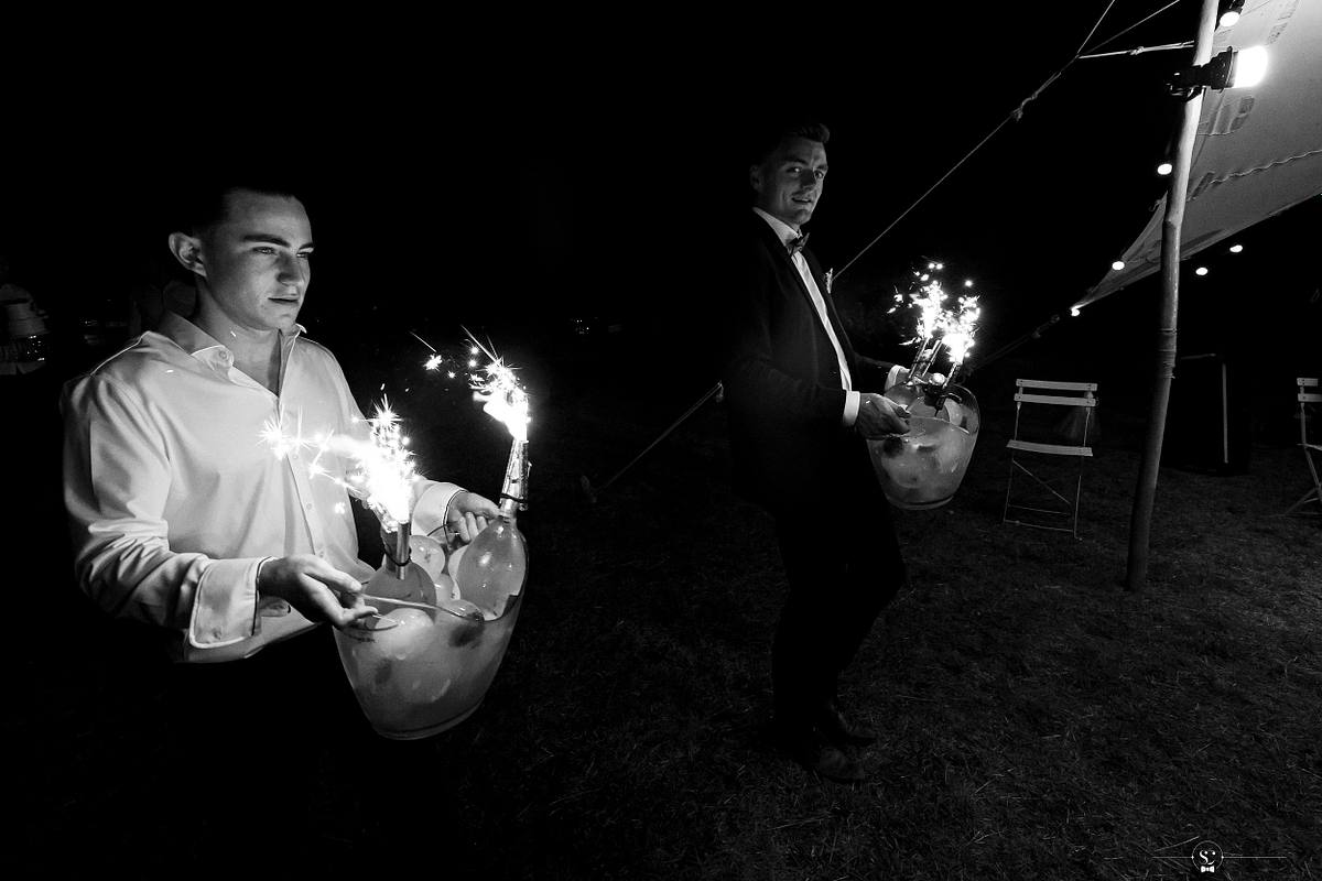 T&eacute;moins du mari&eacute; entrant avec des seaux de champagne illumin&eacute;s pendant la soir&eacute;e sous la tente apr&egrave;s la C&eacute;r&eacute;monie La&iuml;que sous le soleil de Sommi&egrave;res. Mariage N&icirc;mes - Occitanie. Sebastien Clavel Photographe Mariage Lyon