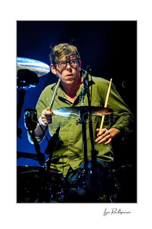 Vertical color image of Patrick Carney of The Black Keys playing drums in close-up under cool blue stage lighting