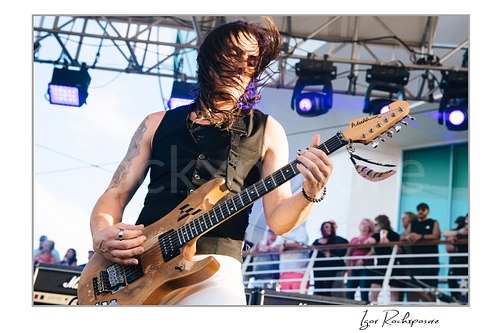 Horizontal color image of Nuno Bettencourt performing live on stage with an electric guitar and windblown hair across his face